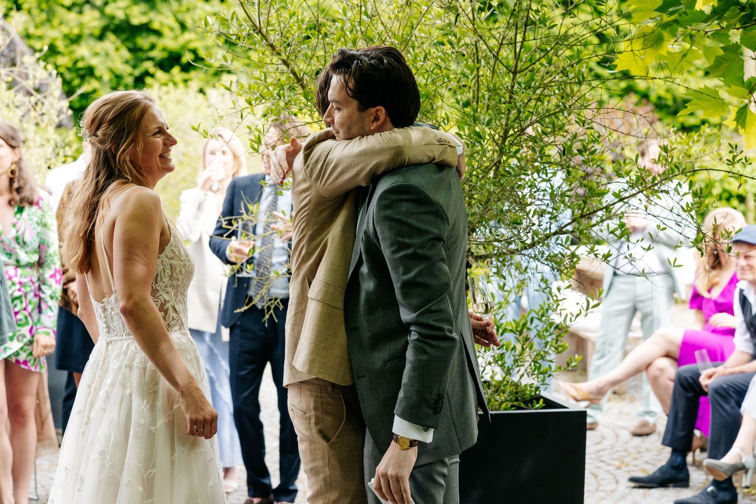 Bride in backless gown embracing a guest during an outdoor wedding reception.