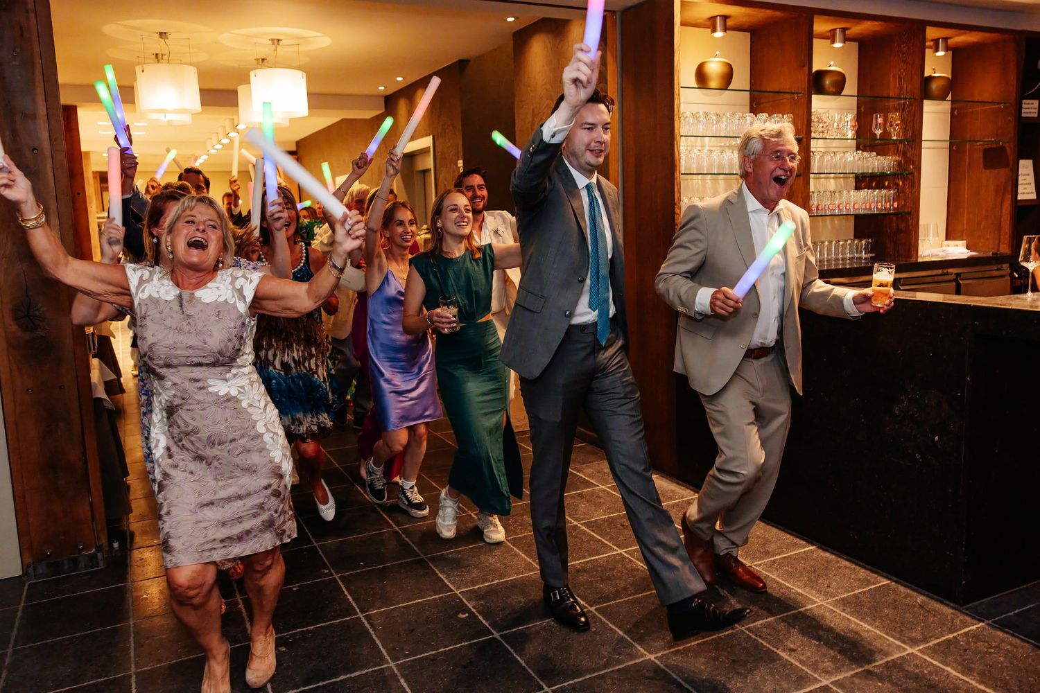 Excited wedding guests waving glow sticks as they enter a hotel reception venue in celebration.