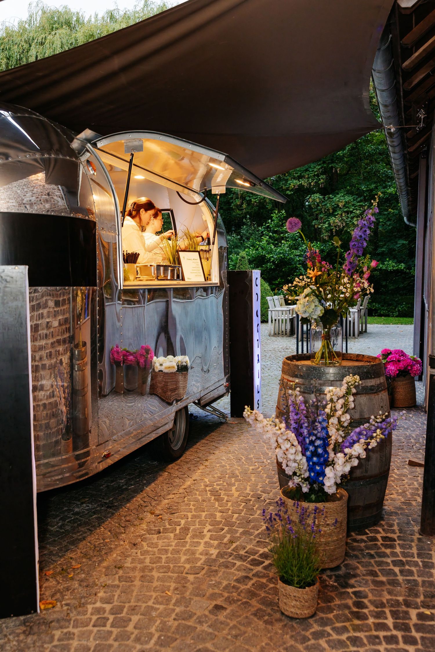 Vintage Airstream food truck with floral barrel decorations serves guests at outdoor wedding reception.