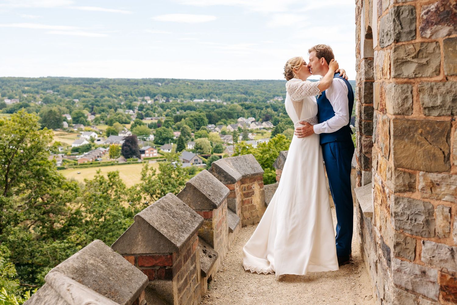 Bride and groom sharing a romantic kiss on a stone castle wall with scenic countryside views.