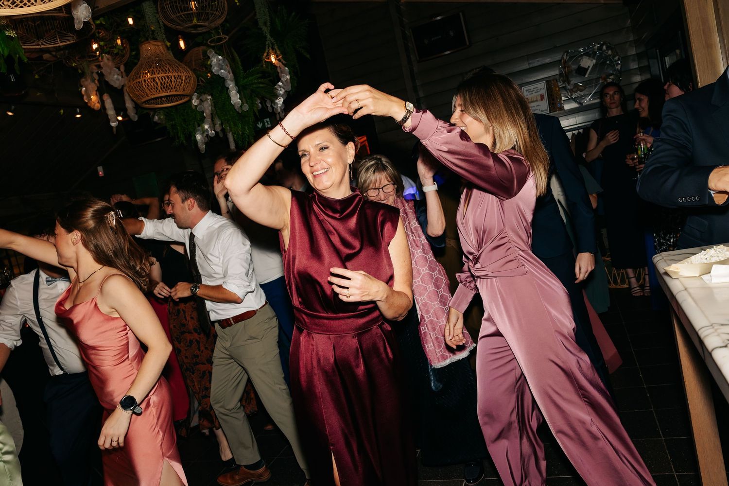Guests in elegant satin outfits dancing energetically at a lively wedding reception party.