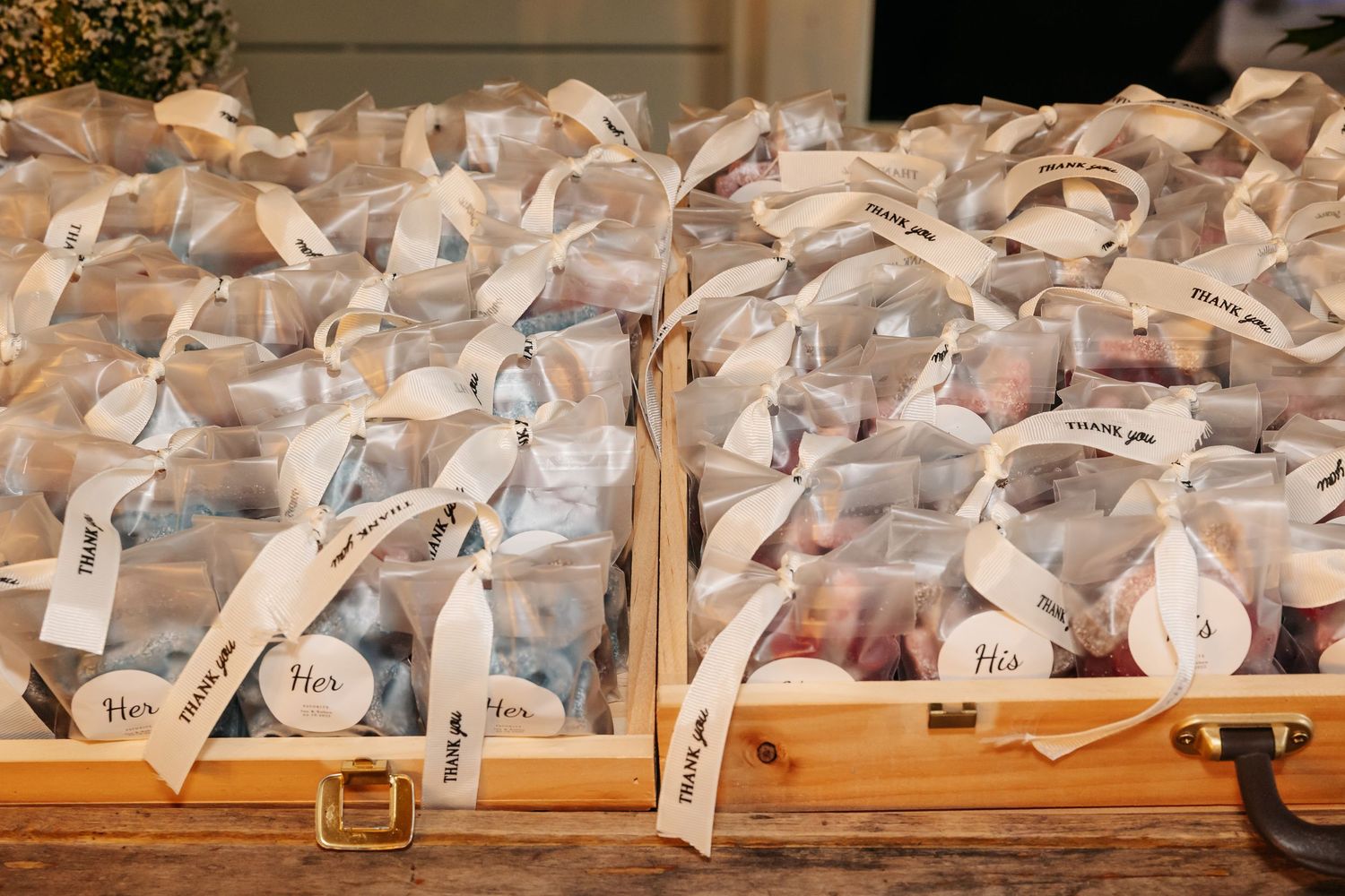 Elegant wedding favor bags tied with white ribbons labeled His and Hers displayed in wooden boxes.