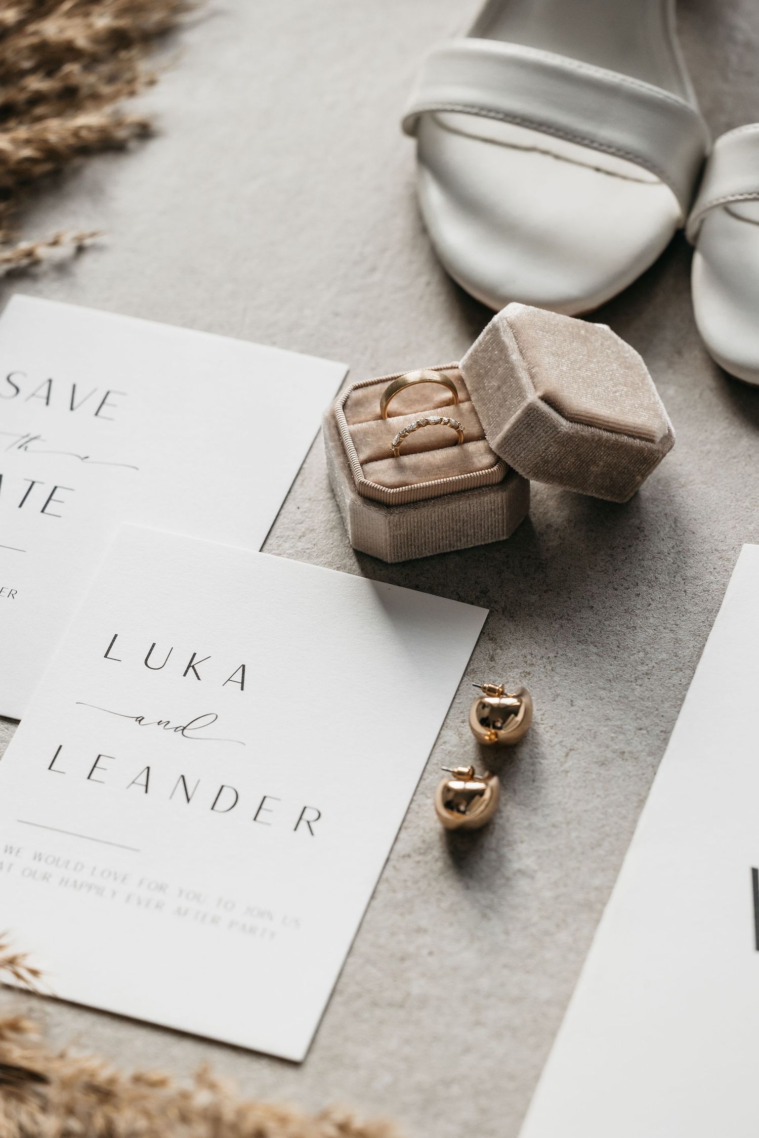 Elegant wedding flat lay featuring invitation suite, gold rings in velvet box, earrings and bridal heels.