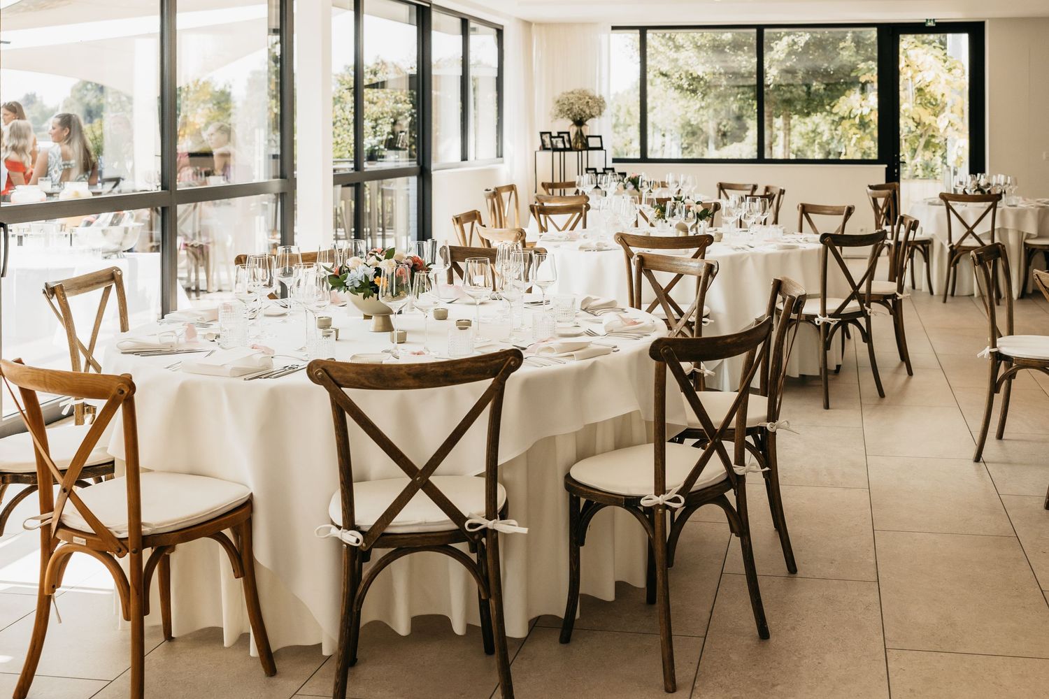 Elegant wedding reception venue with white tablecloths, cross-back wooden chairs, and floral centerpieces.