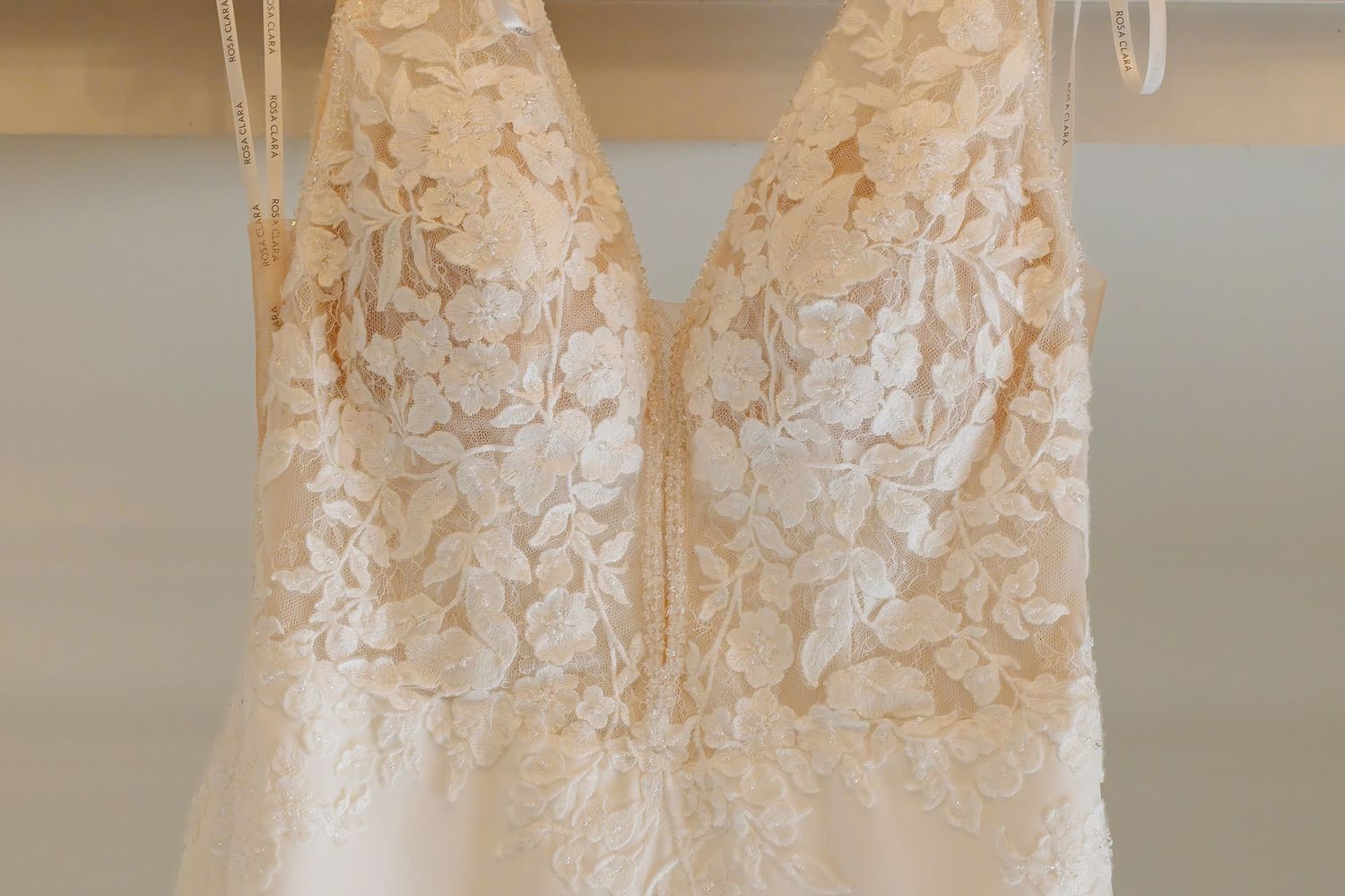 Close-up of a sleeveless ivory wedding dress bodice featuring intricate floral lace detailing on a hanger.