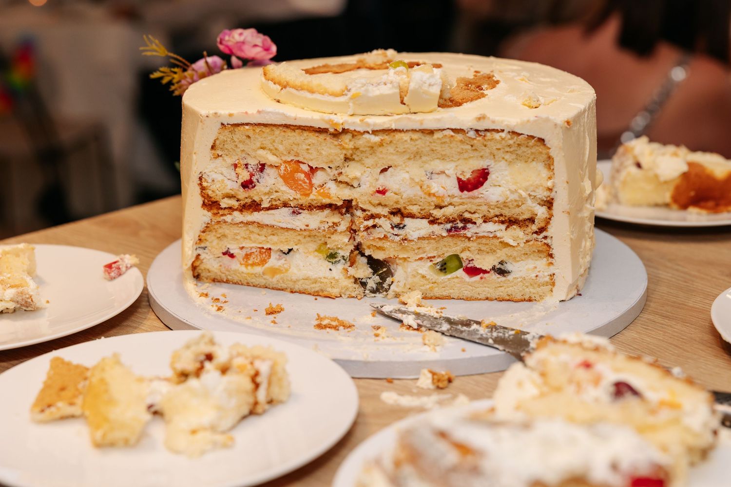 Sliced multi-layer white wedding cake with fruit filling on wooden table.