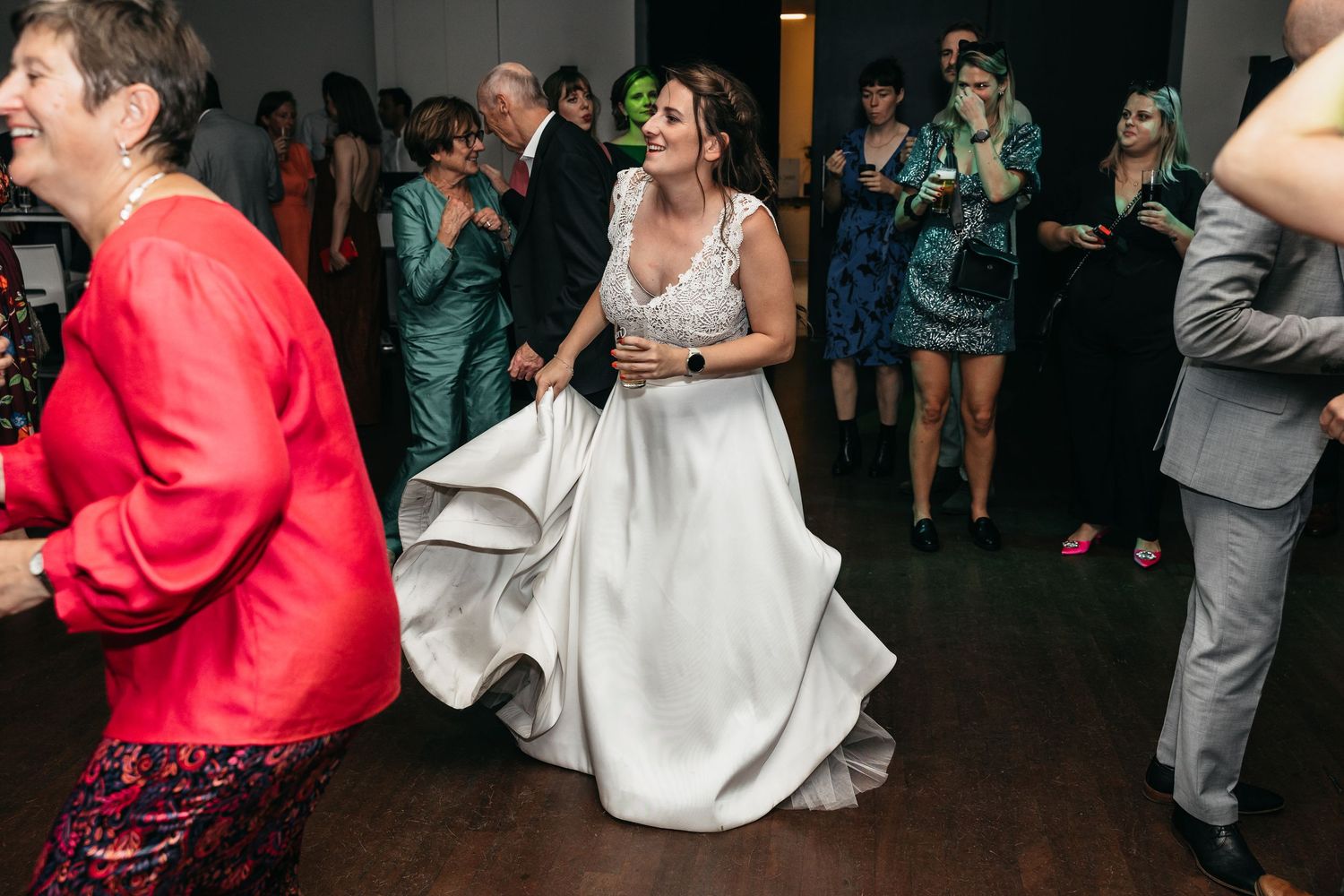 Bride in white gown dancing joyfully at wedding reception surrounded by guests.