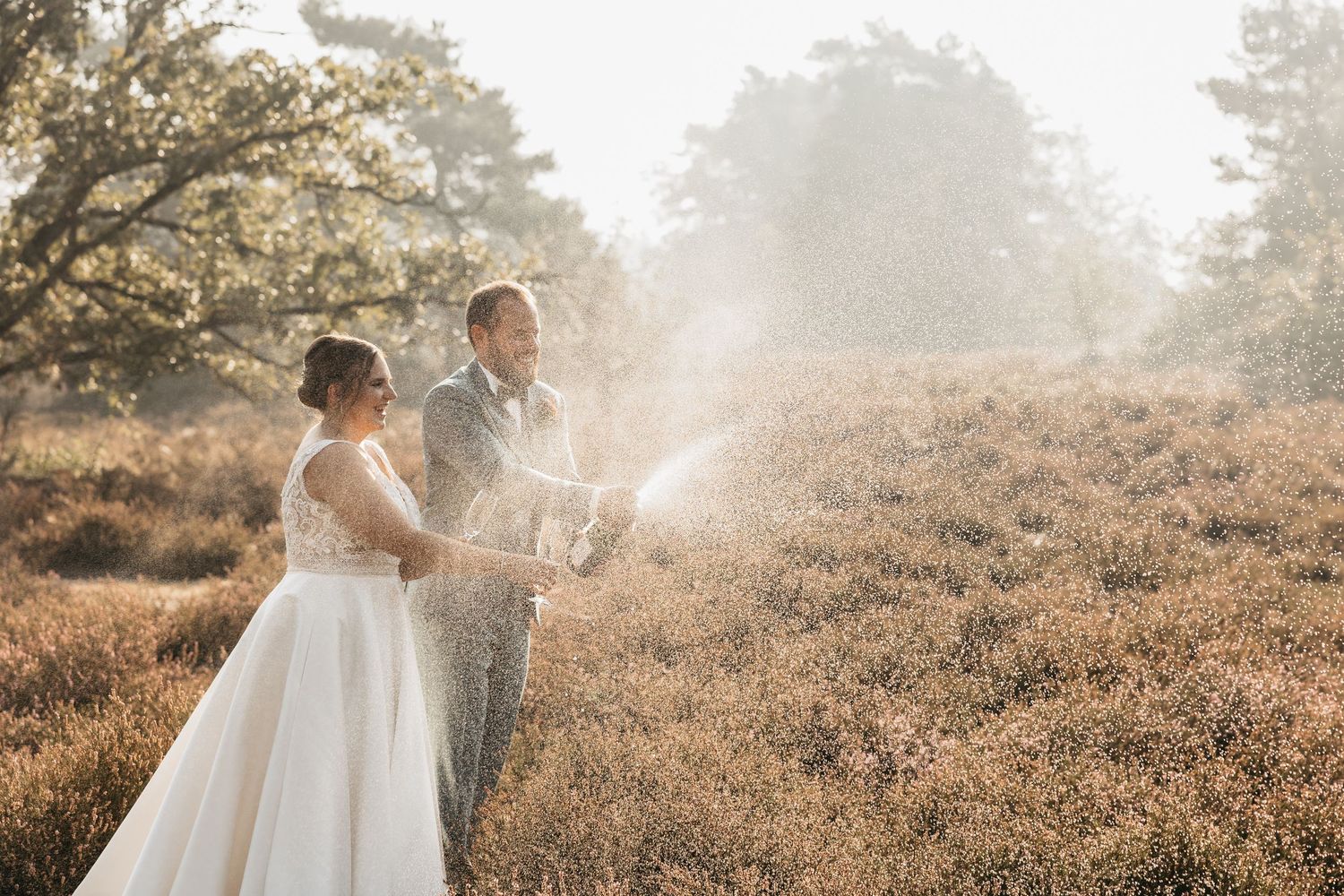 Bride and groom popping champagne in a golden heather field with misty trees in the background.