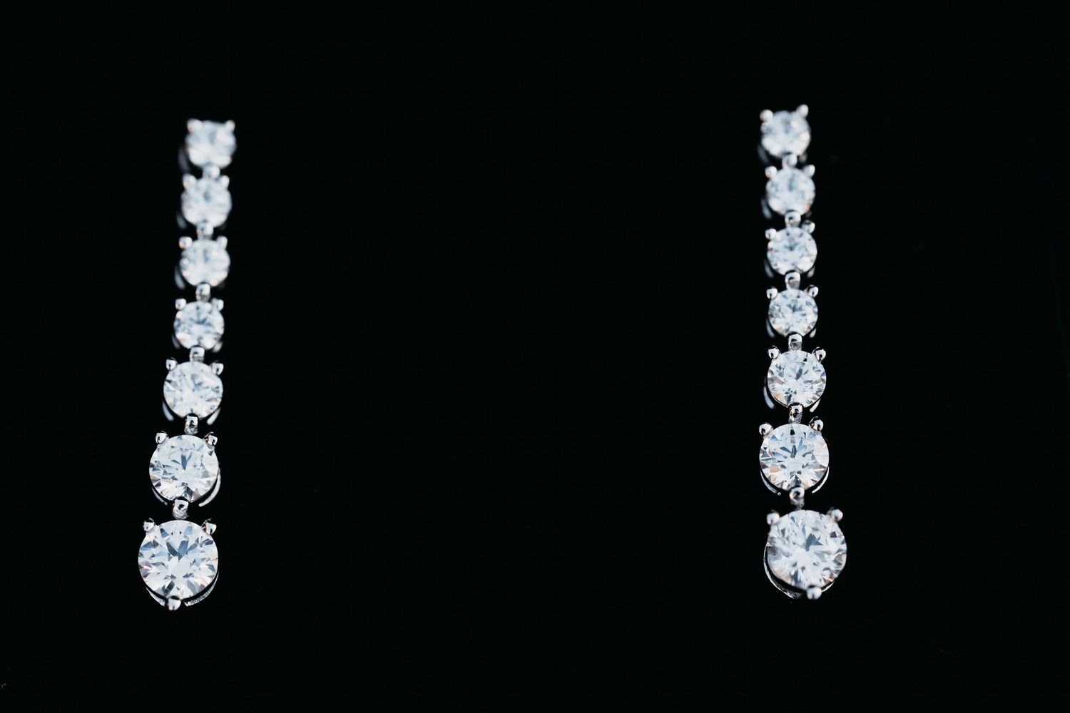 Elegant diamond drop earrings with graduated round stones in silver setting against black background.