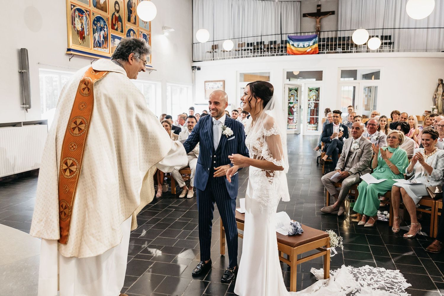Bride and groom standing before priest during traditional church wedding ceremony with guests.