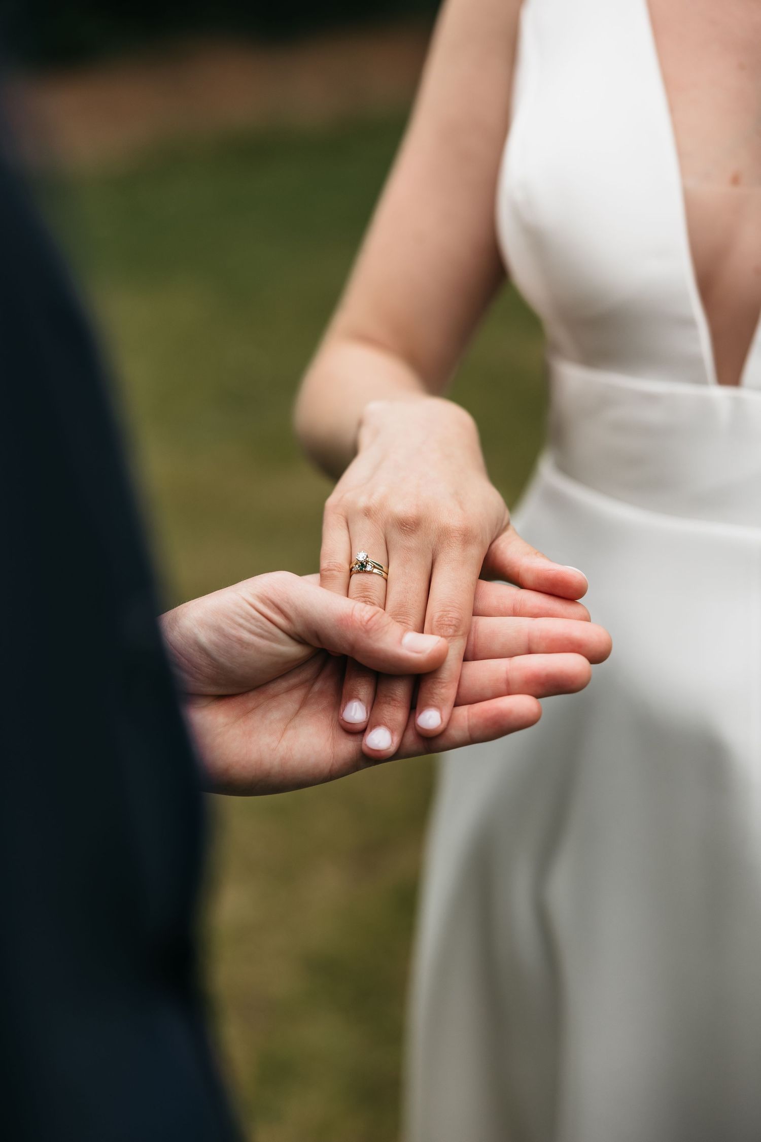 Close-up of bride and groom holding hands, showcasing elegant engagement ring on wedding day.