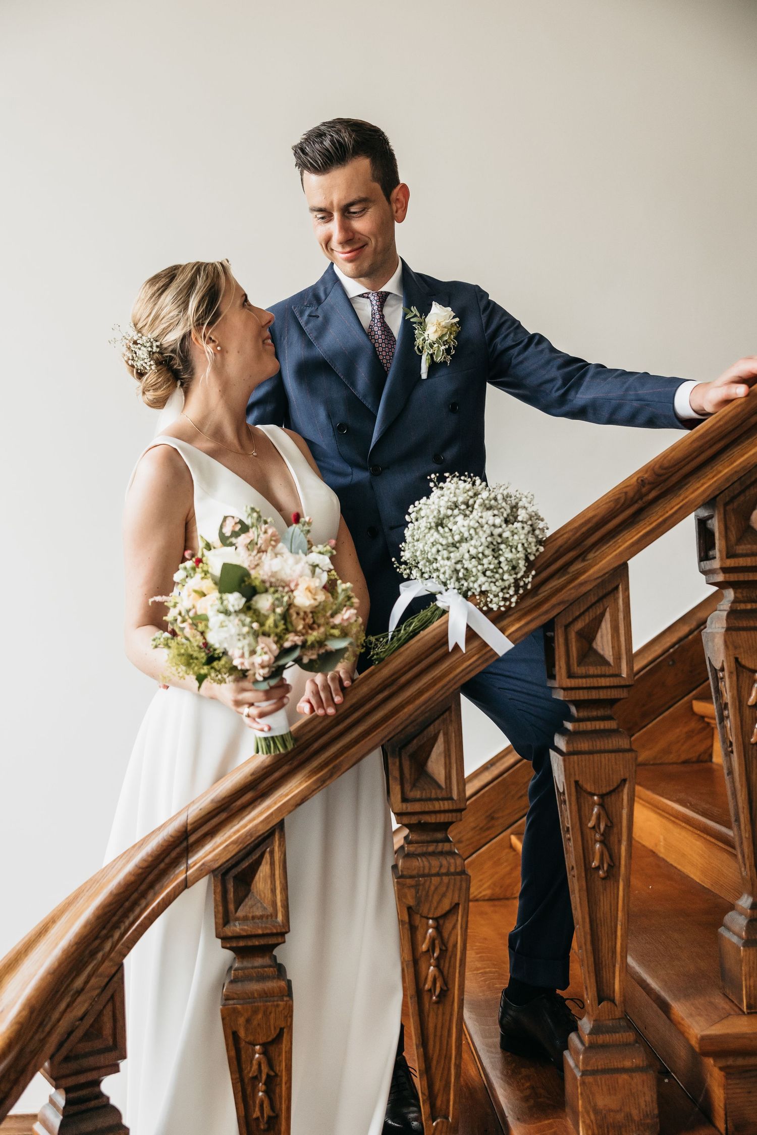 Bride and groom sharing a romantic moment on elegant wooden staircase, groom smiling down at bride with bouquet.