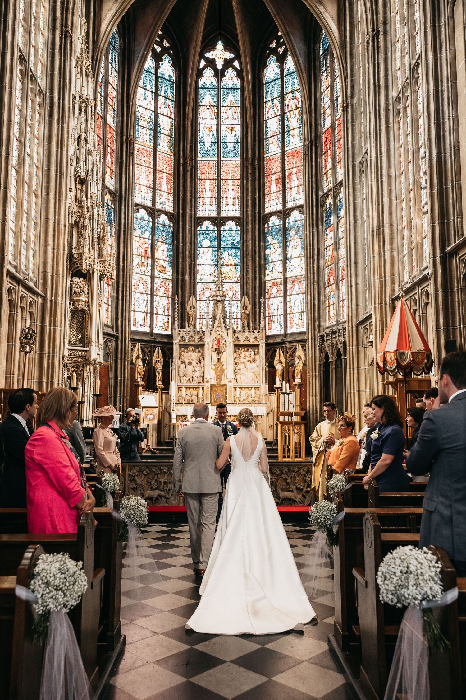 Bride walking down the aisle of a stunning Gothic cathedral with stained glass windows and floral decorations.