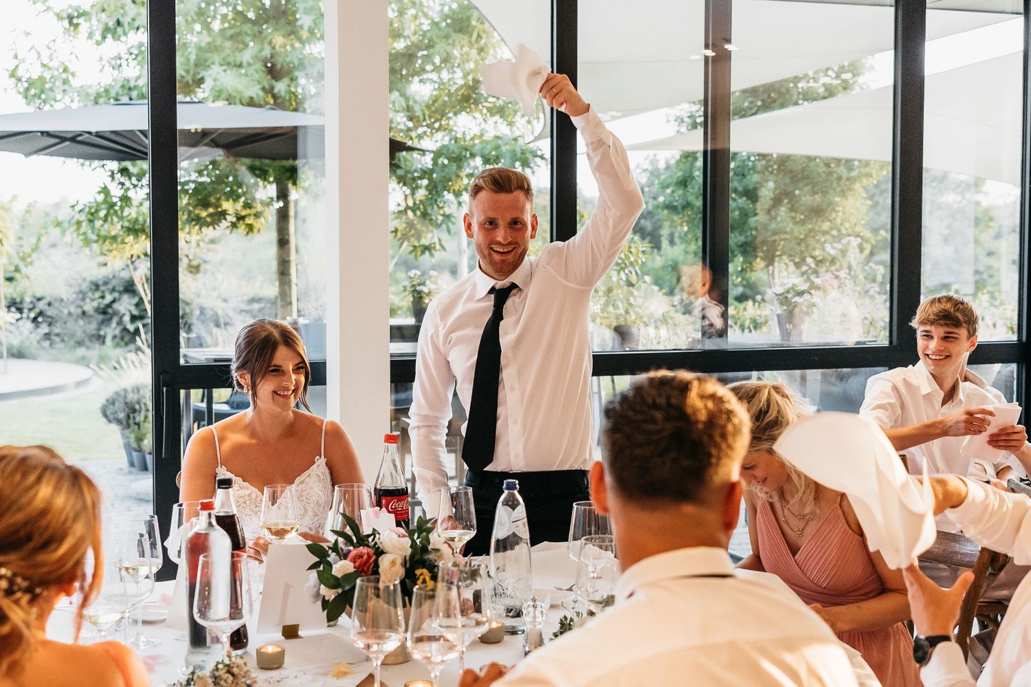Groom standing and waving napkin at wedding reception head table.