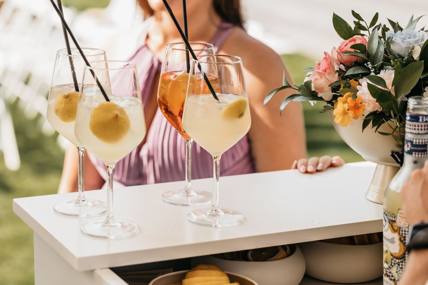 Elegant wine glasses with citrus garnishes displayed on a white bar cart at outdoor wedding.