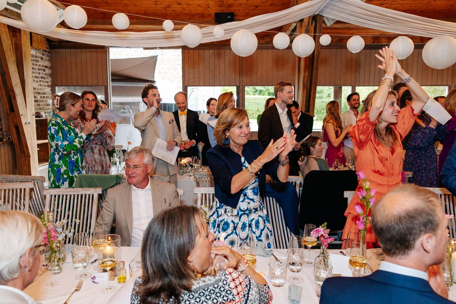 Wedding reception guests clapping and celebrating at elegantly decorated venue with white paper lantern decorations.