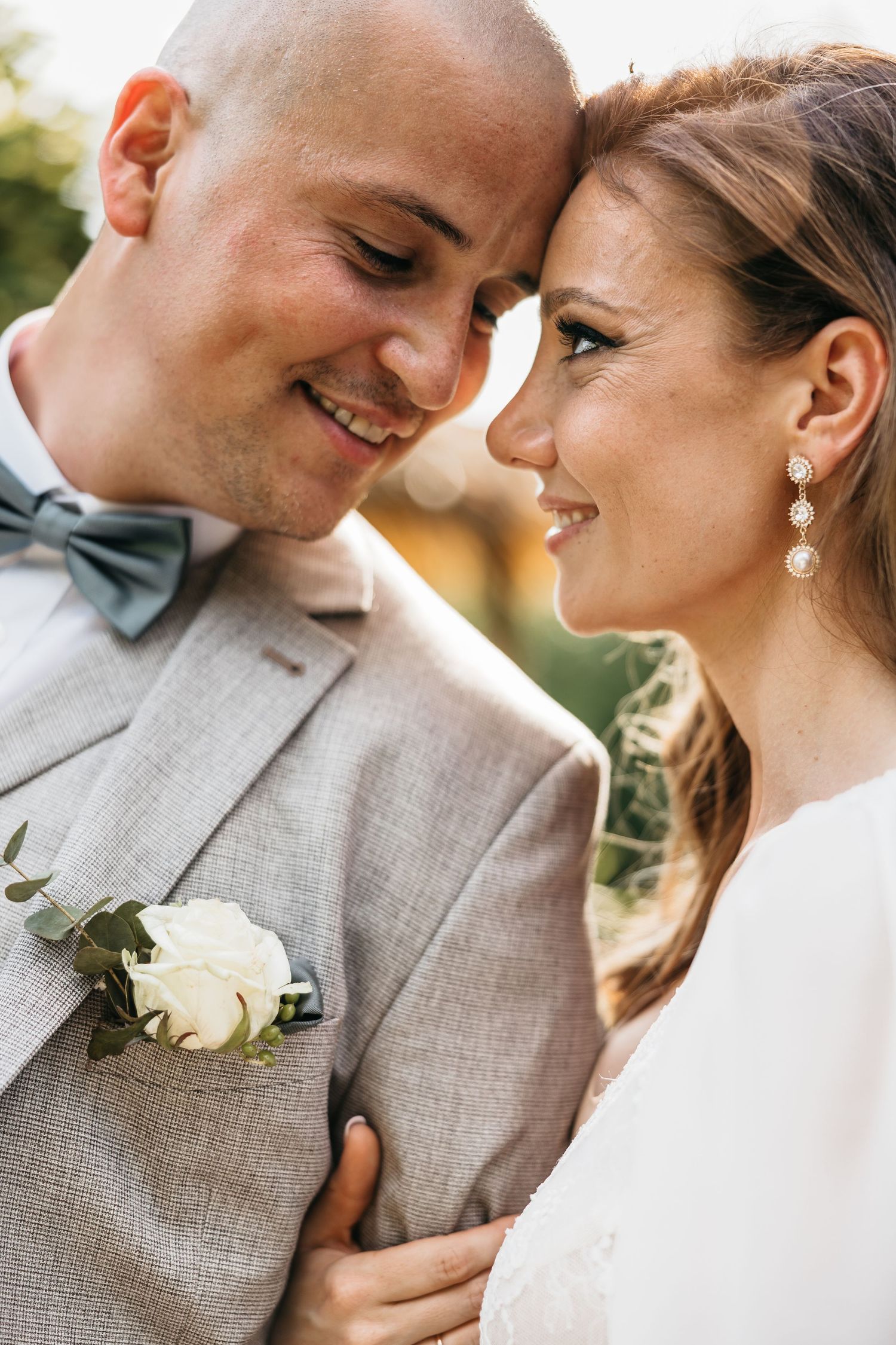 Joyful bride and groom sharing an intimate smile, groom wearing gray suit with white rose boutonniere.