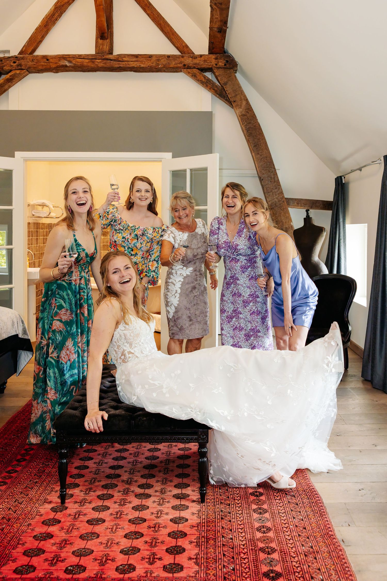 Excited bridesmaids and family celebrating with bride in white wedding gown in rustic venue.