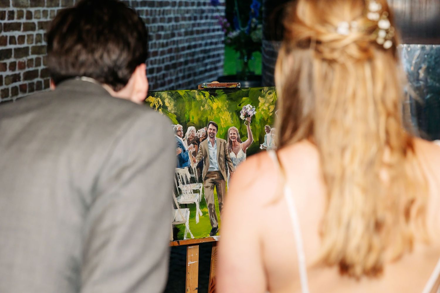 Couple views completed live wedding painting showing ceremony moment on canvas at reception venue.