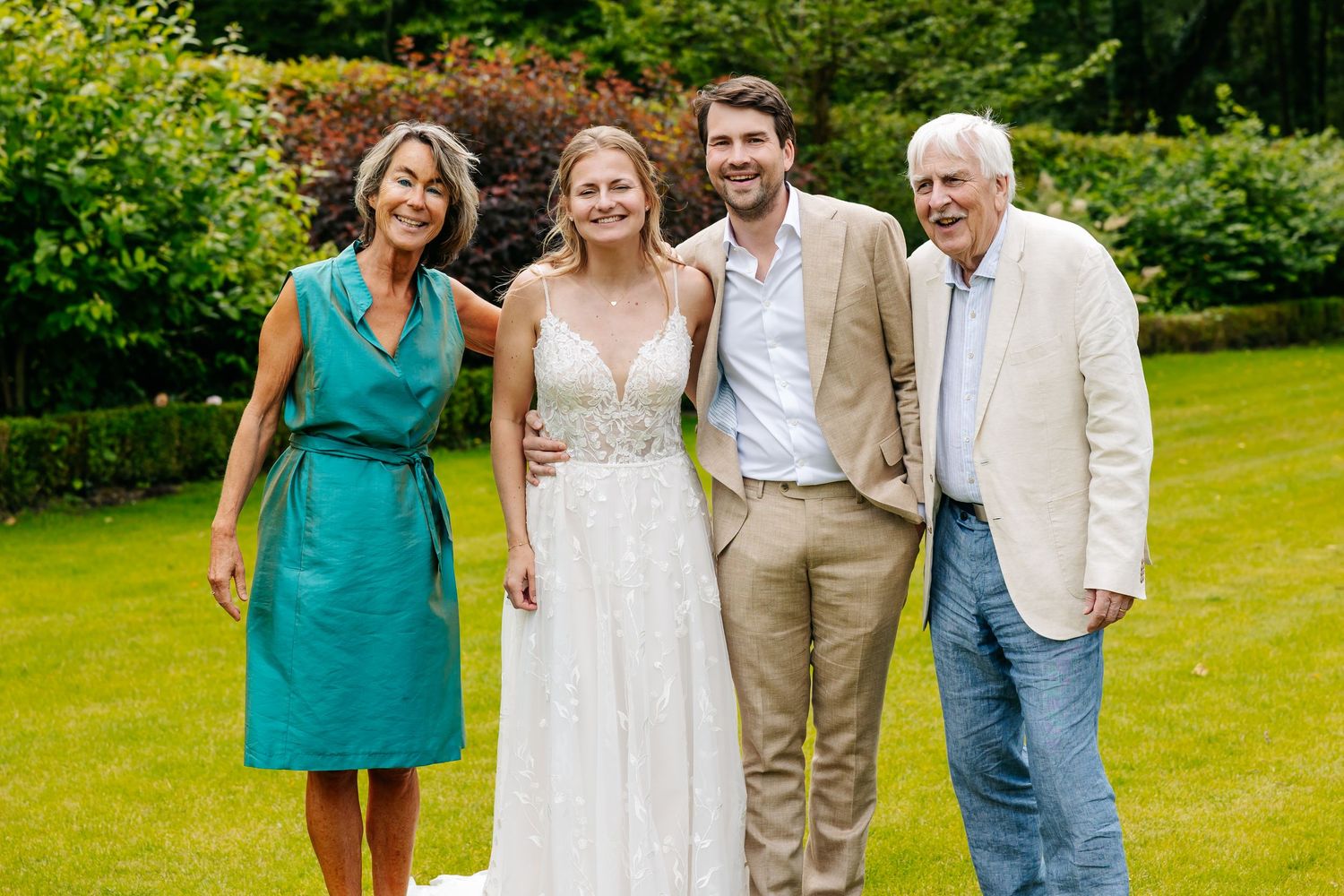 Bride and groom smiling with older couple in garden during outdoor wedding celebration.