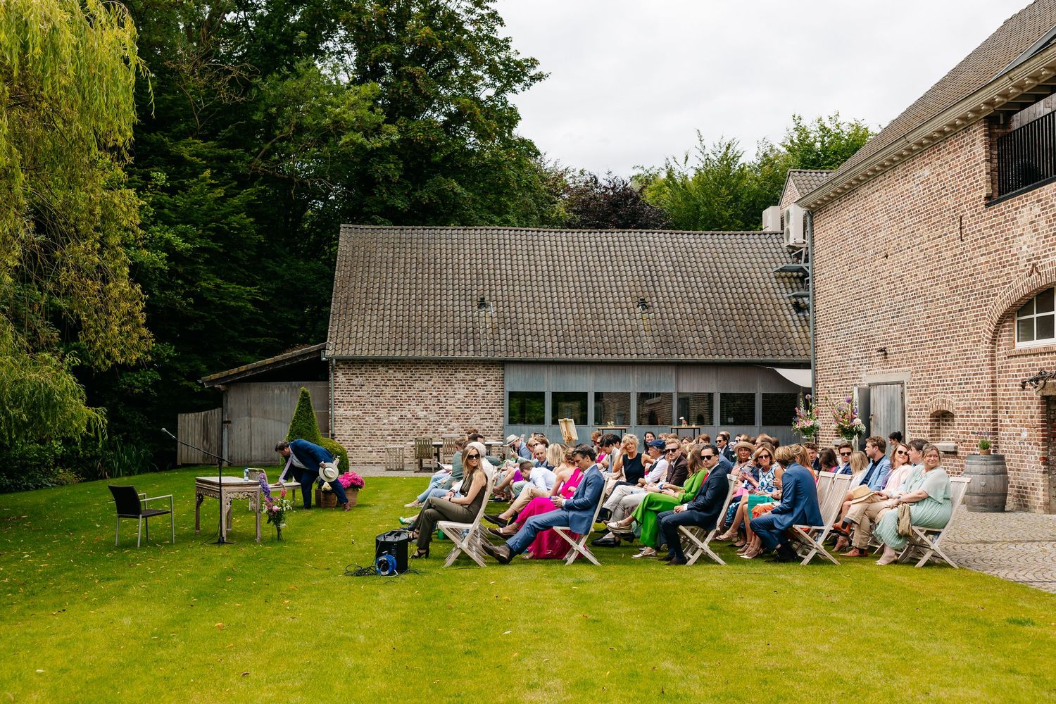 Wedding guests seated in garden chairs on a lush green lawn during an outdoor ceremony.