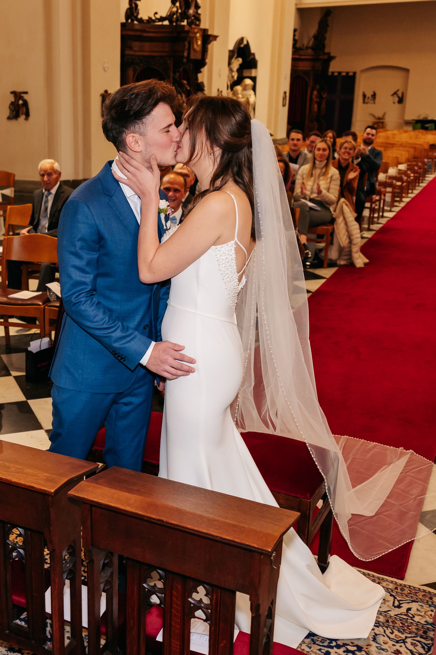Newlywed couple shares first kiss on red carpet aisle in historic church ceremony.