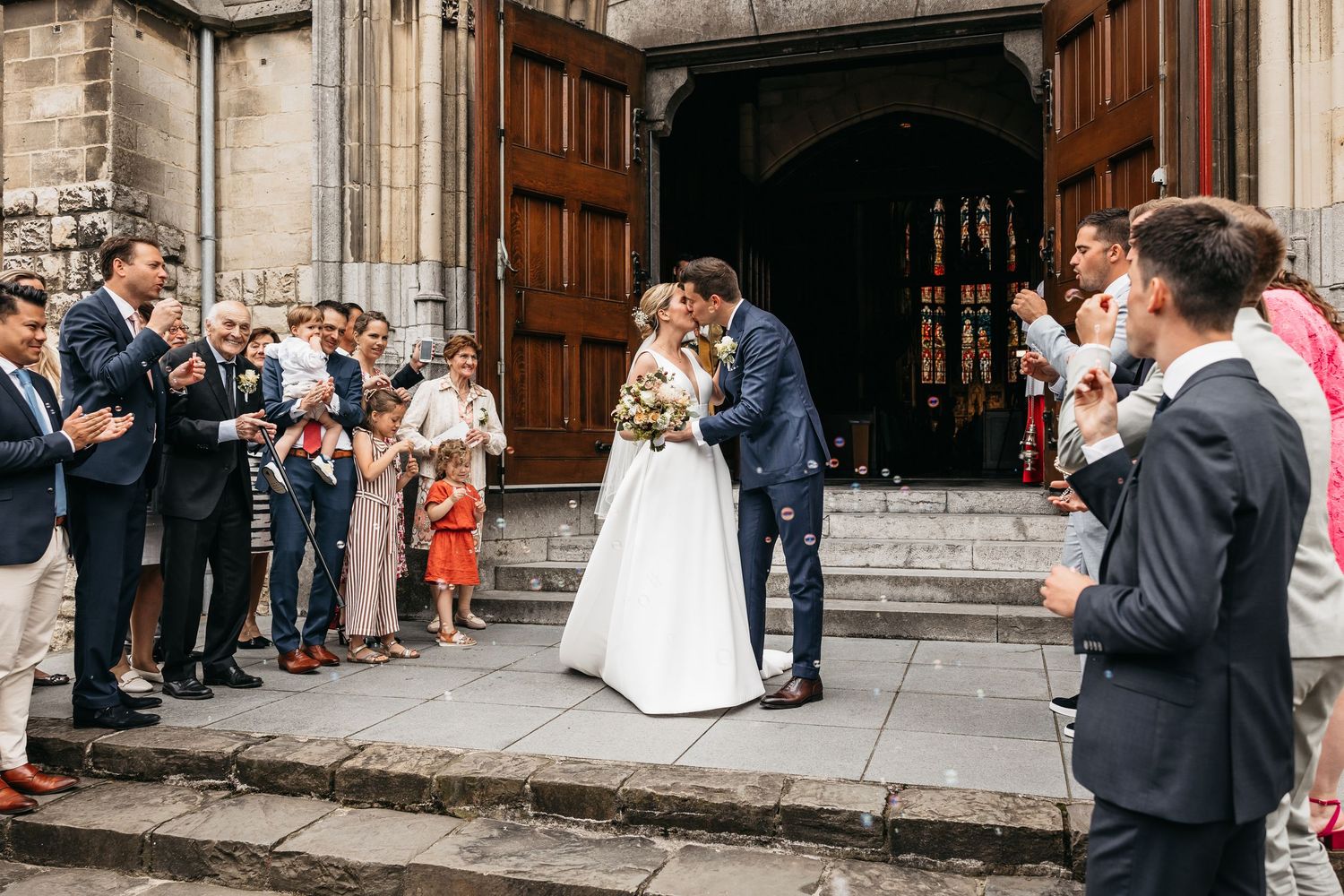 Bride and groom share first kiss outside church surrounded by cheering guests.