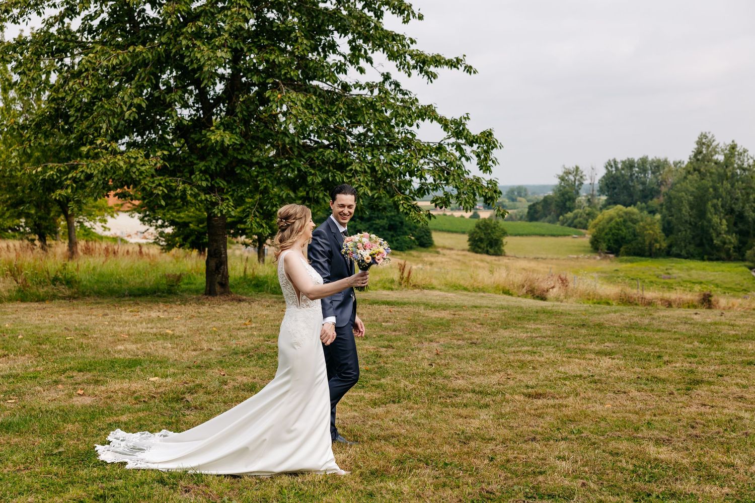 Bride and groom walking together in a scenic green field on their wedding day.