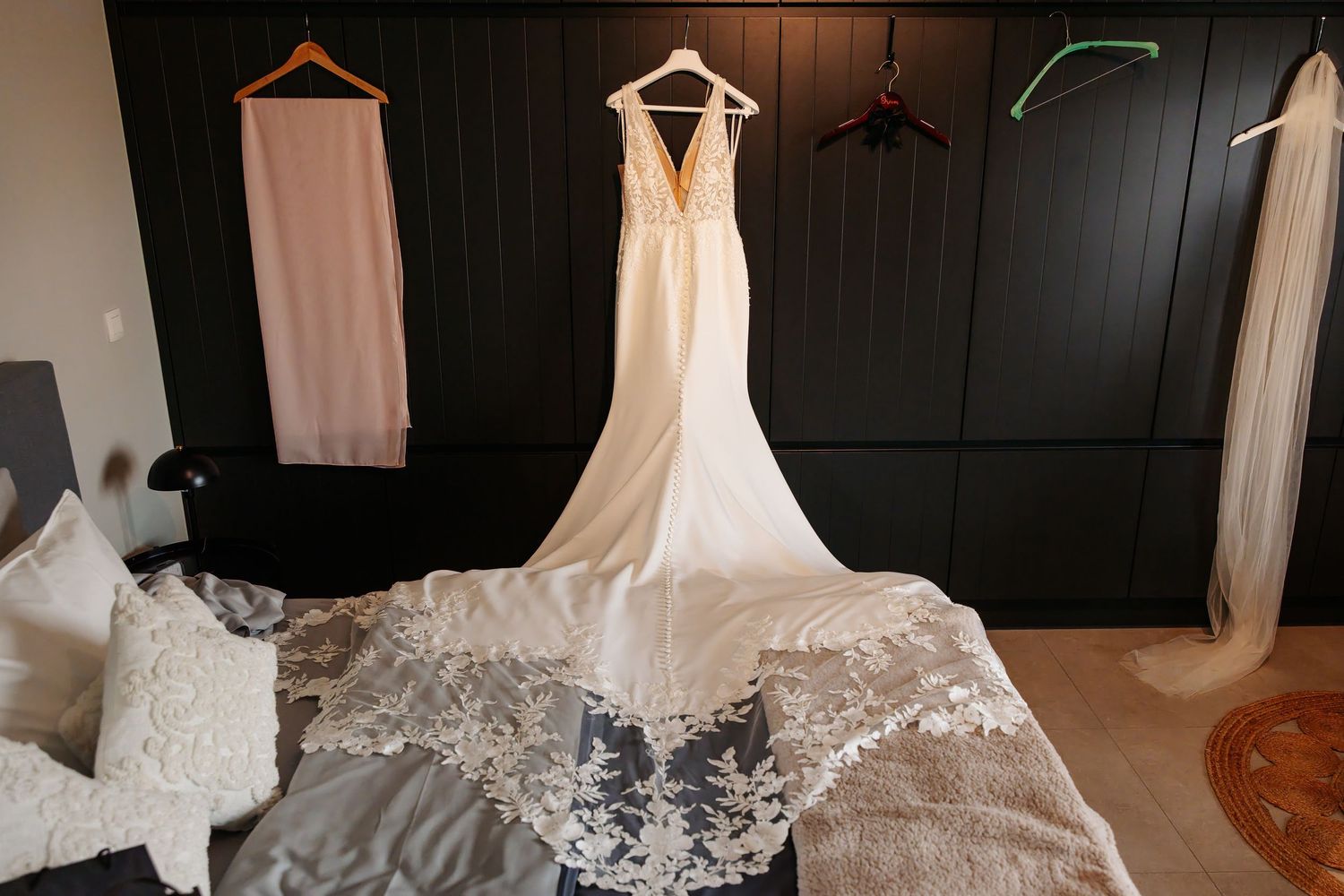 Elegant lace-train wedding dress hanging in a modern bedroom with additional bridal attire.