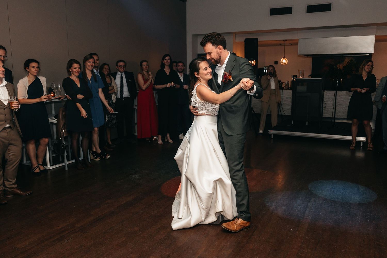 Bride and groom slow dance together as wedding guests watch from the sidelines.