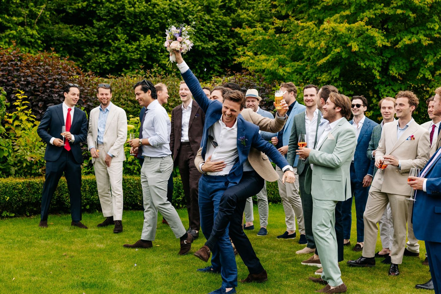 Excited groomsman catches bridal bouquet while celebrating with friends at a wedding.