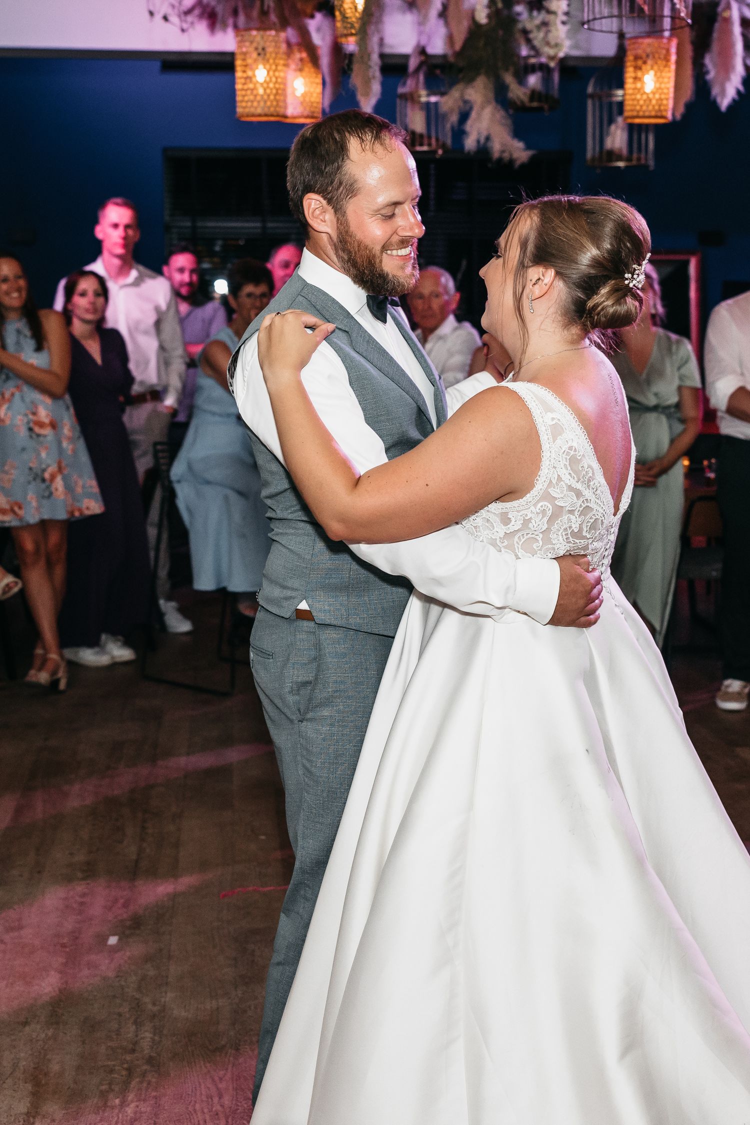 Smiling groom in grey vest holds his bride close during an intimate first dance at their wedding reception.