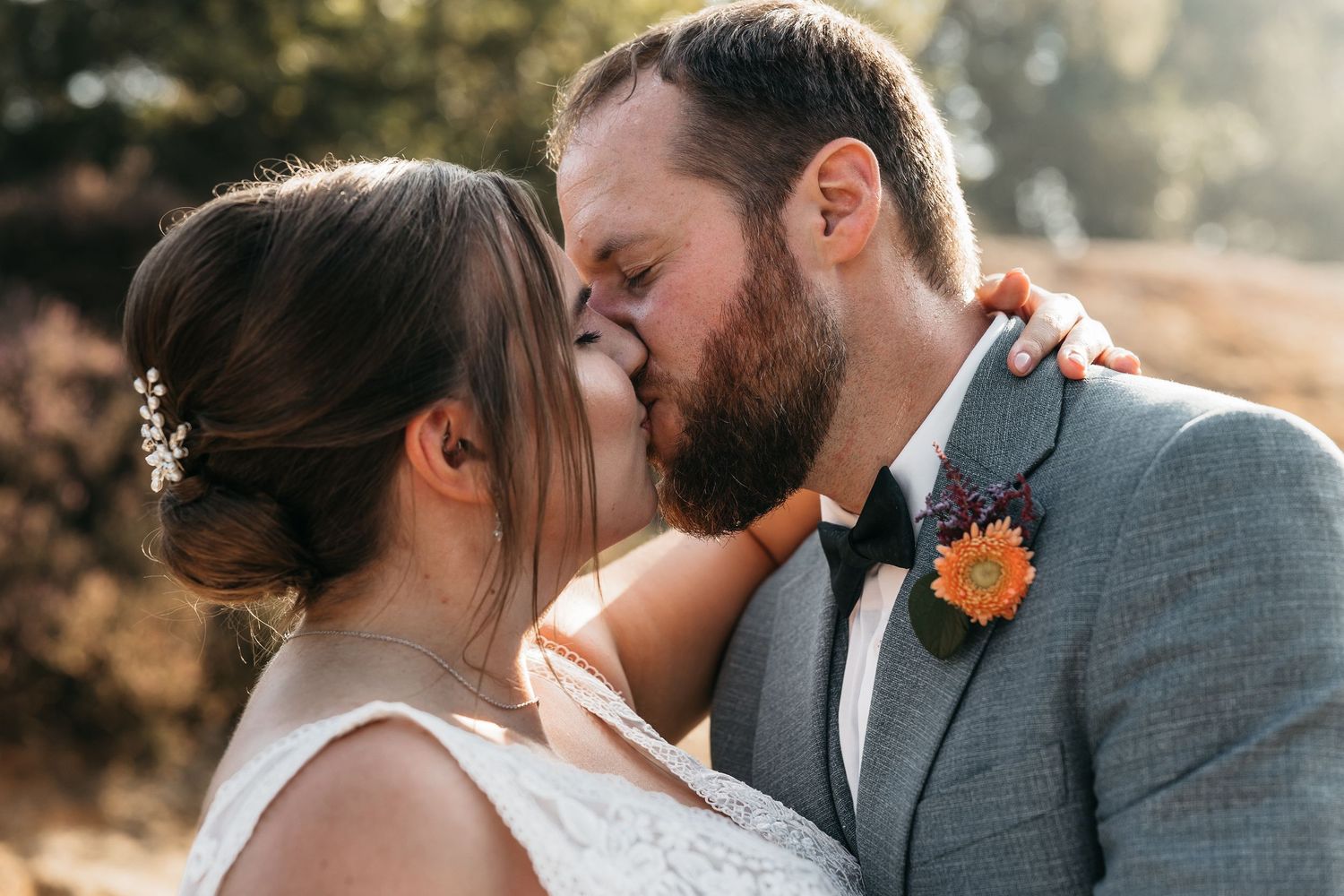 Bride and groom sharing a romantic kiss outdoors with groom wearing an orange boutonniere.