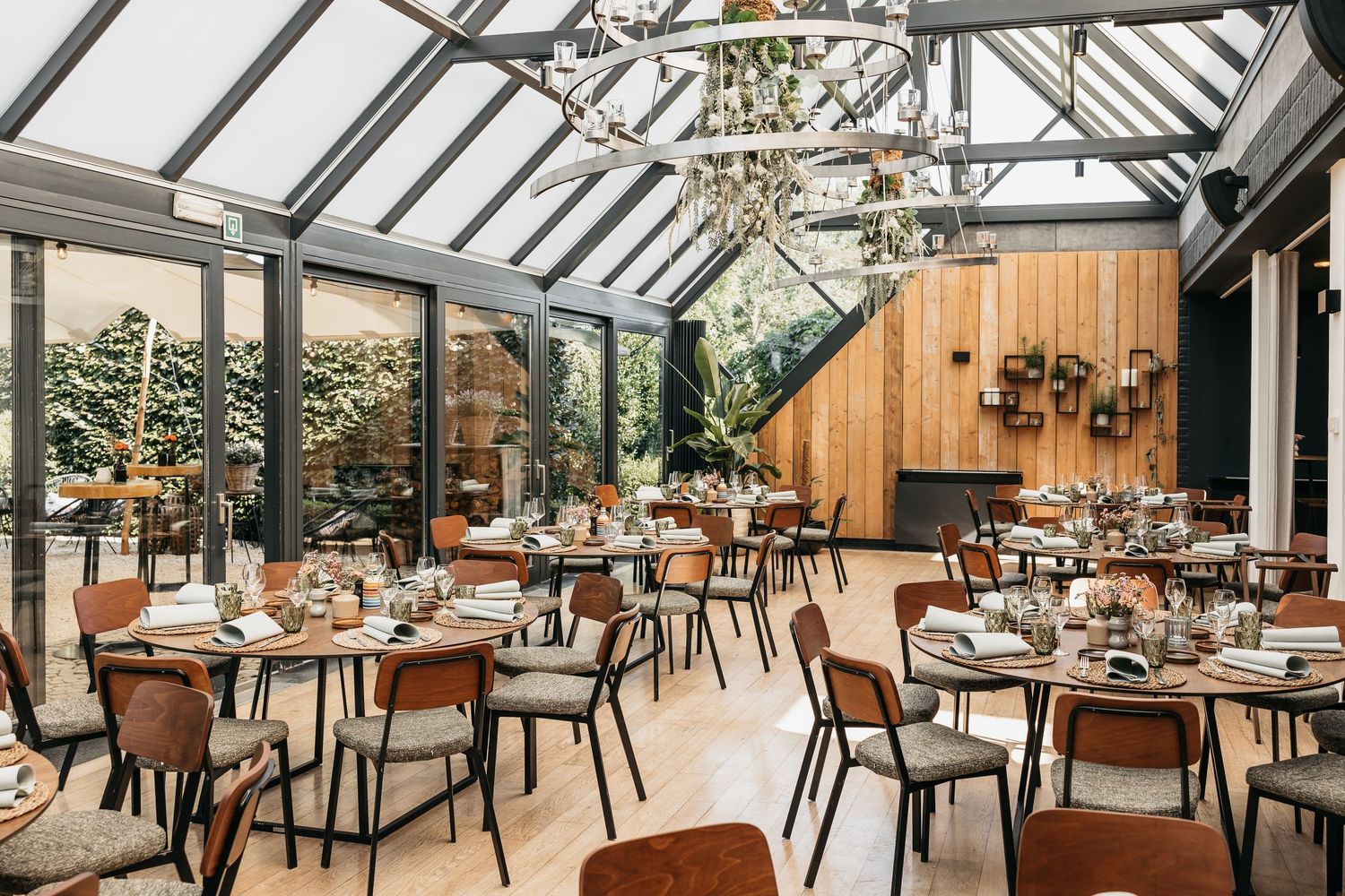 Elegant glass-roof conservatory dining room with chandelier, set tables, and warm wooden accents for a wedding reception.