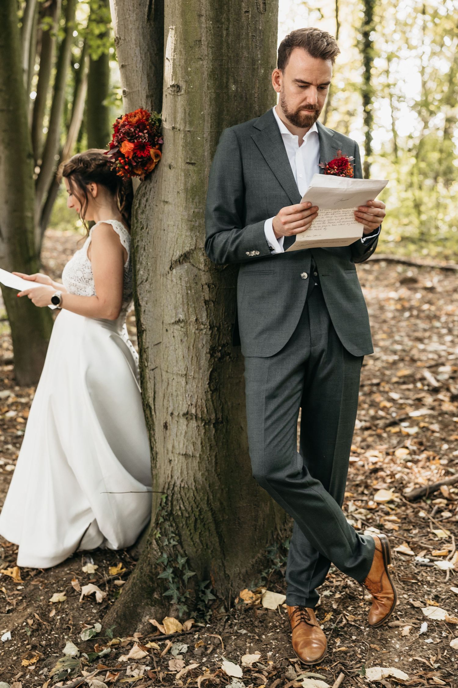 Bride and groom standing on opposite sides of a tree privately reading their wedding vow letters.