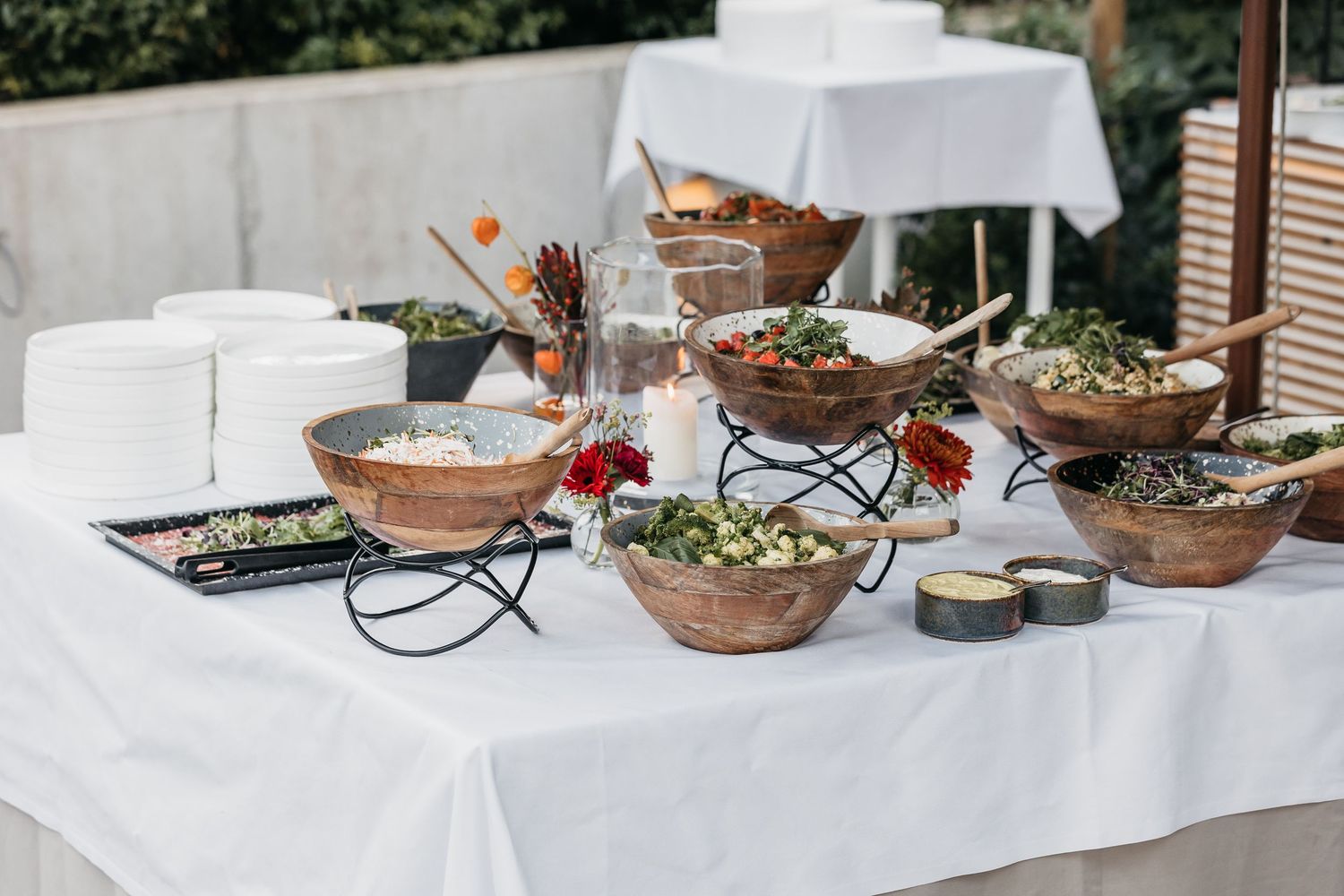Elegant outdoor buffet table with wooden bowls of fresh salads on a white linen tablecloth.