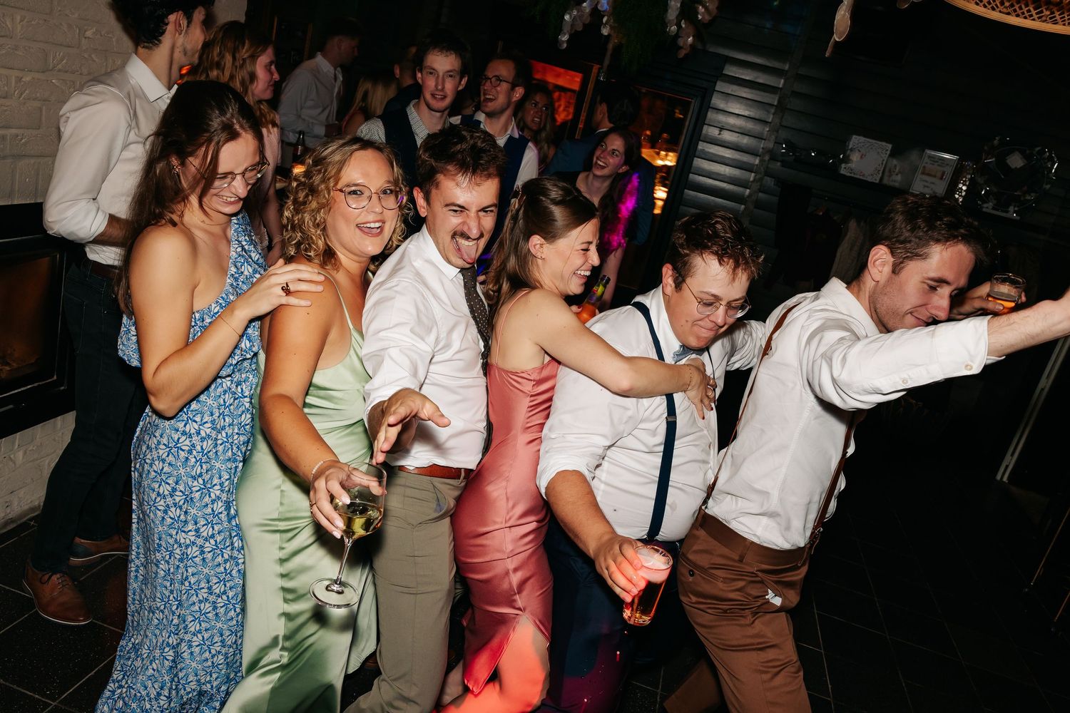 Cheerful wedding guests posing and dancing together at a fun evening reception celebration.