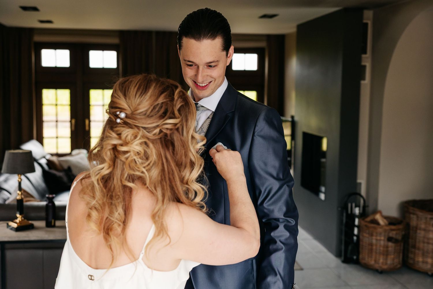 Bride adjusting groom's navy suit lapel as he smiles down at her lovingly.
