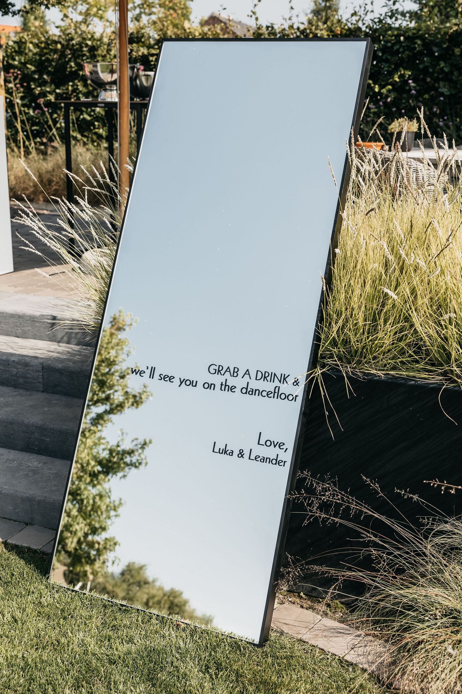 Elegant mirror wedding sign reading Grab a Drink and We'll See You on the Dancefloor, Love Luka and Leander.