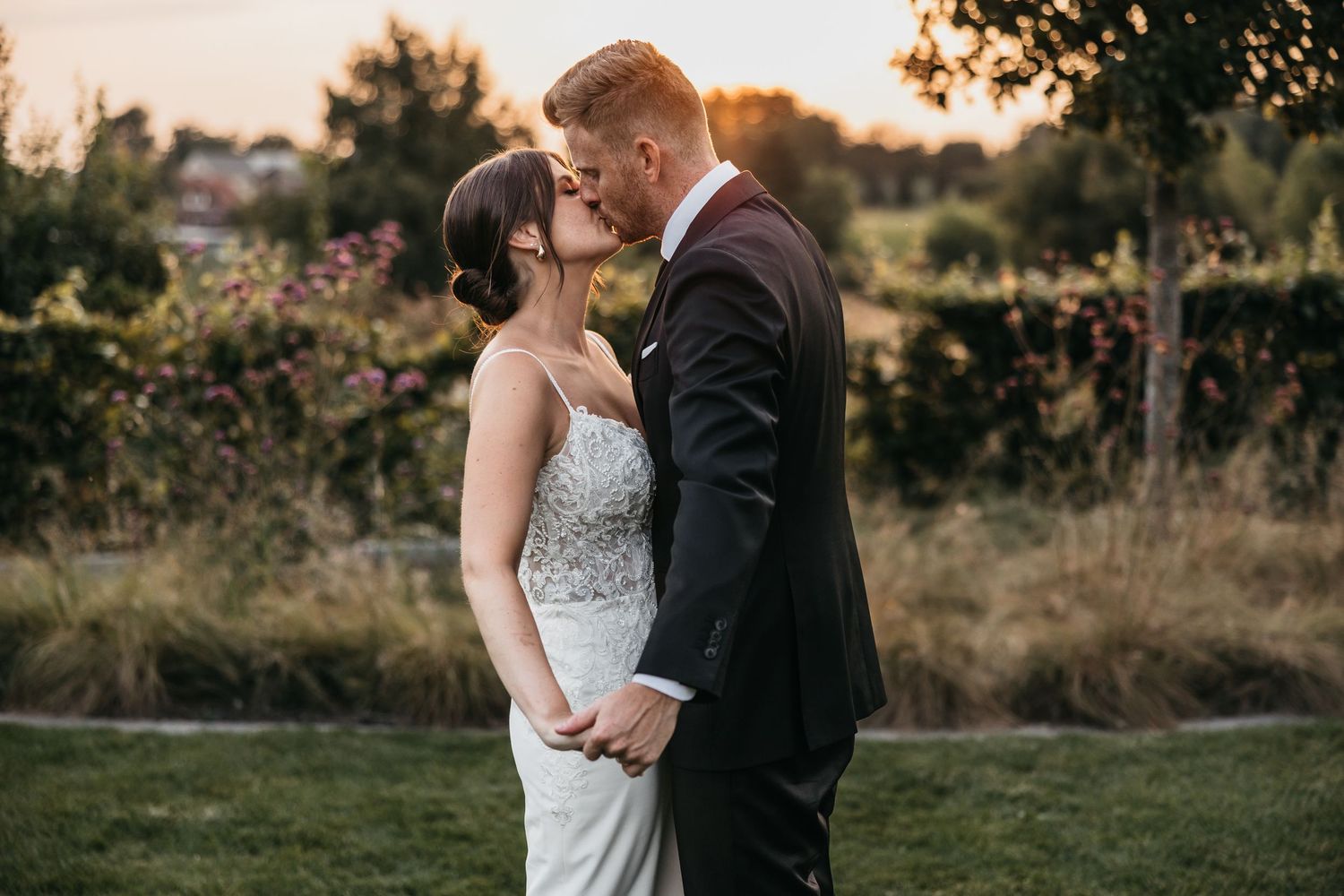 Bride and groom sharing a romantic kiss at golden hour in a lush garden setting.