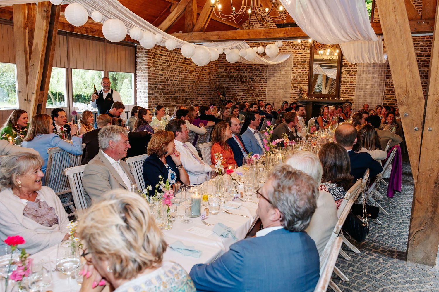 Large wedding reception hall filled with guests seated at elegantly decorated round tables with floral centerpieces.