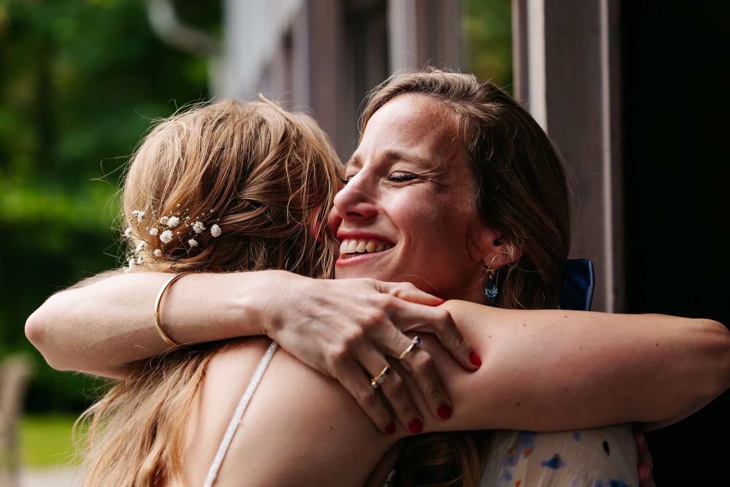 Two women sharing a warm embrace at wedding celebration outdoors.