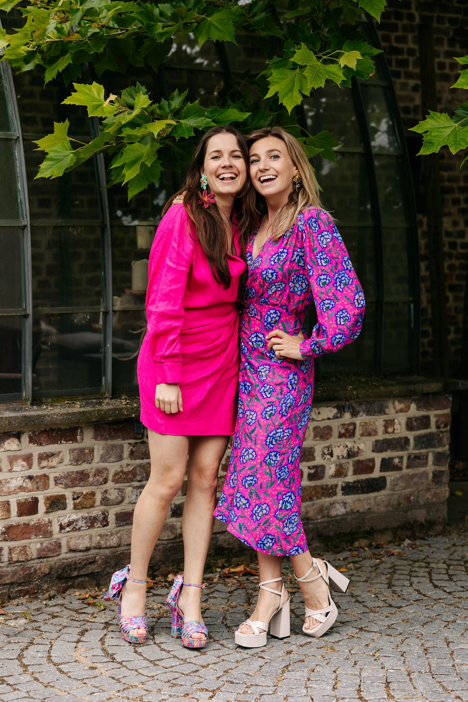 Two women in vibrant pink dresses smiling and posing together at an outdoor wedding.