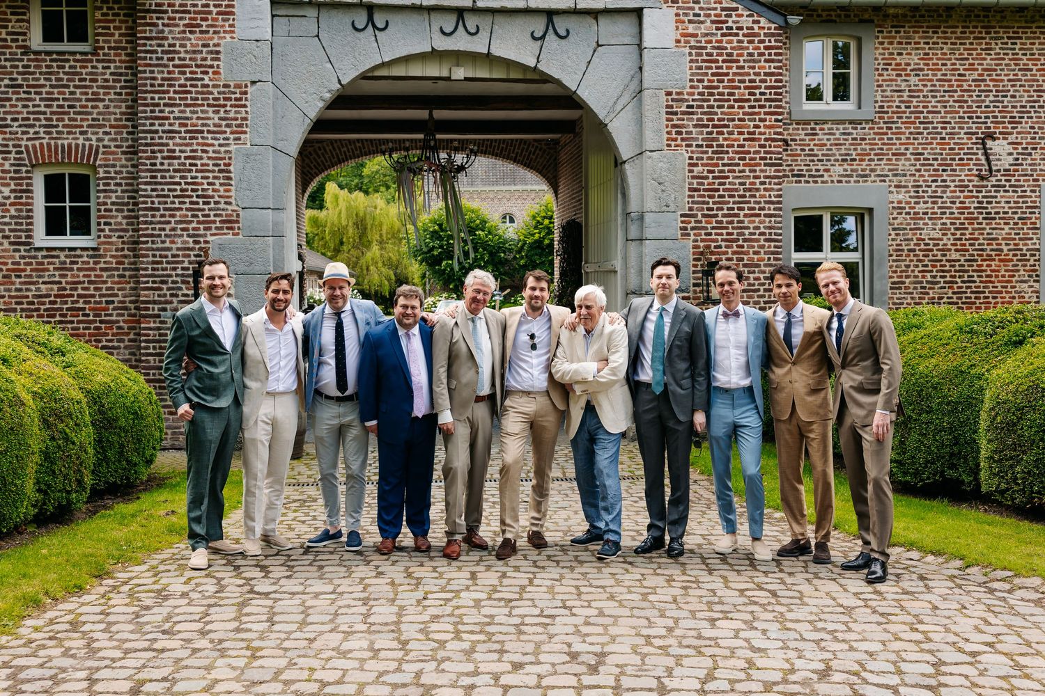 Group of well-dressed men posing together in front of a brick archway outdoors.