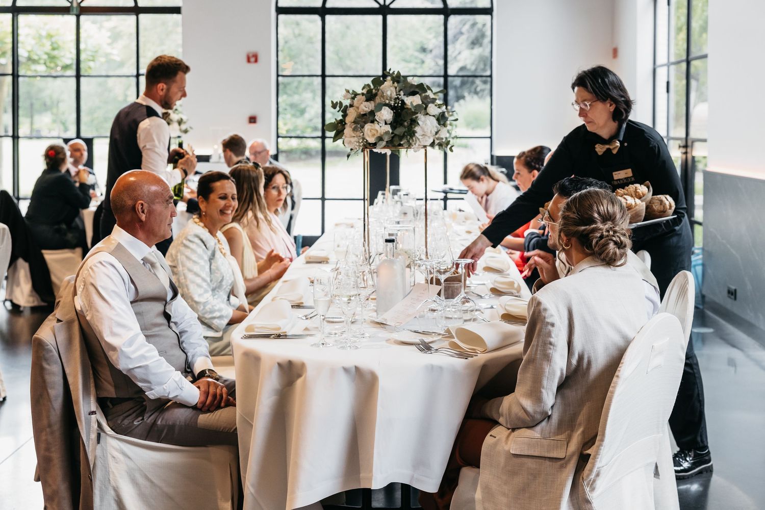 Wedding guests seated at elegantly decorated reception table with floral centerpiece indoors.