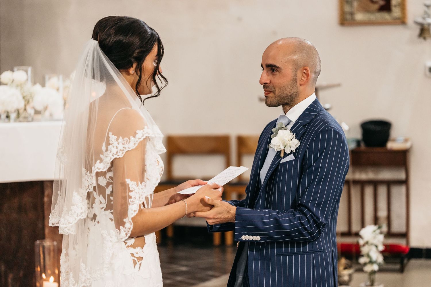 Groom reads wedding vows to bride in lace dress during church ceremony.