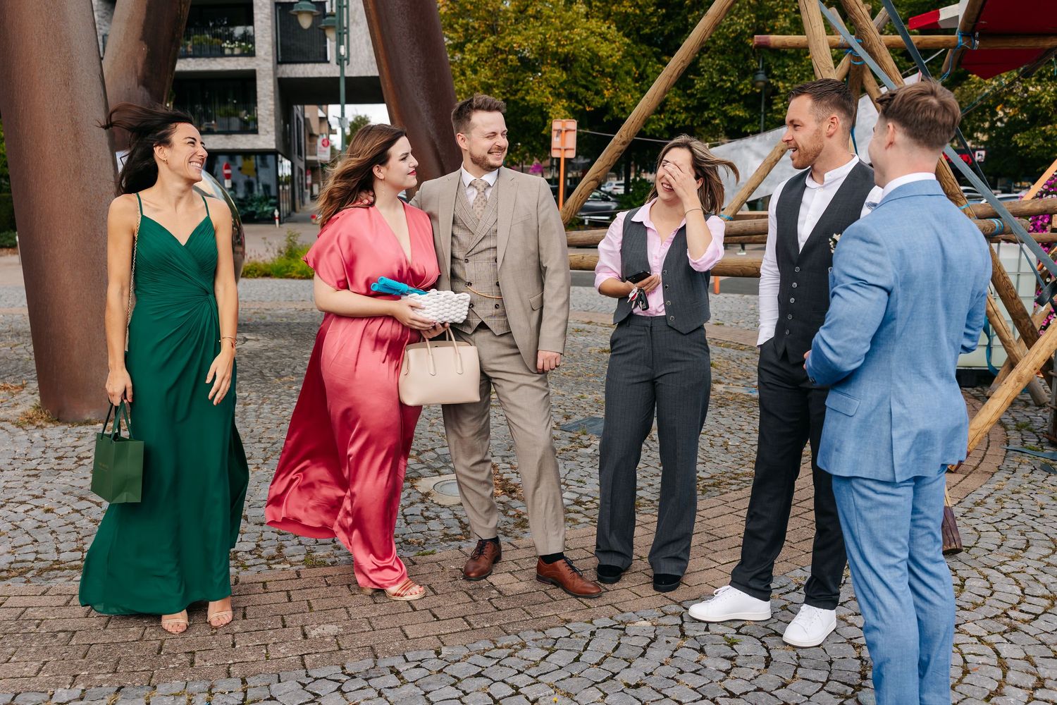 Wedding guests in colorful formal attire socialize outdoors on a cobblestone plaza.