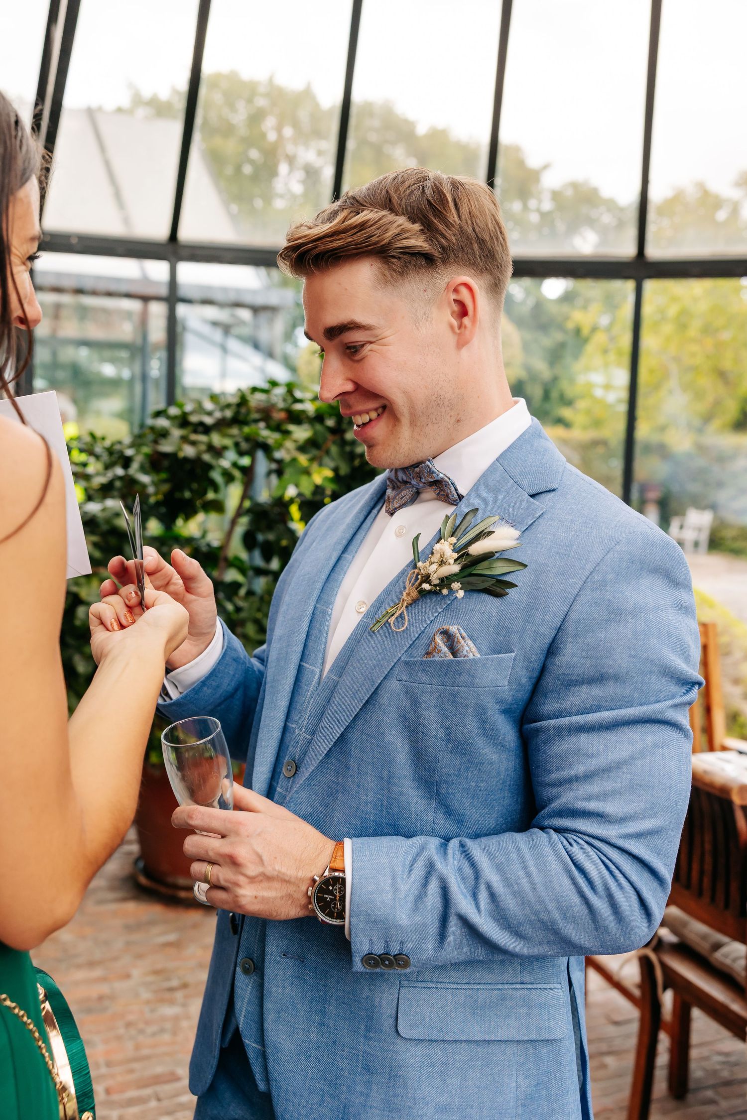 Smiling groom in blue suit with boutonniere holding champagne at wedding reception.