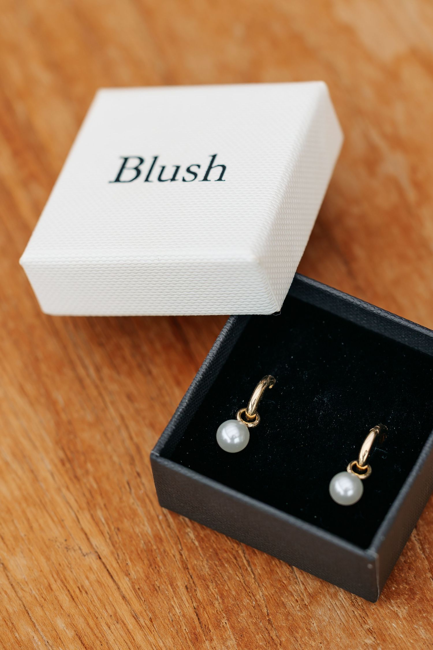 Gold hoop earrings with pearl drops displayed in a Blush jewelry box on wood.