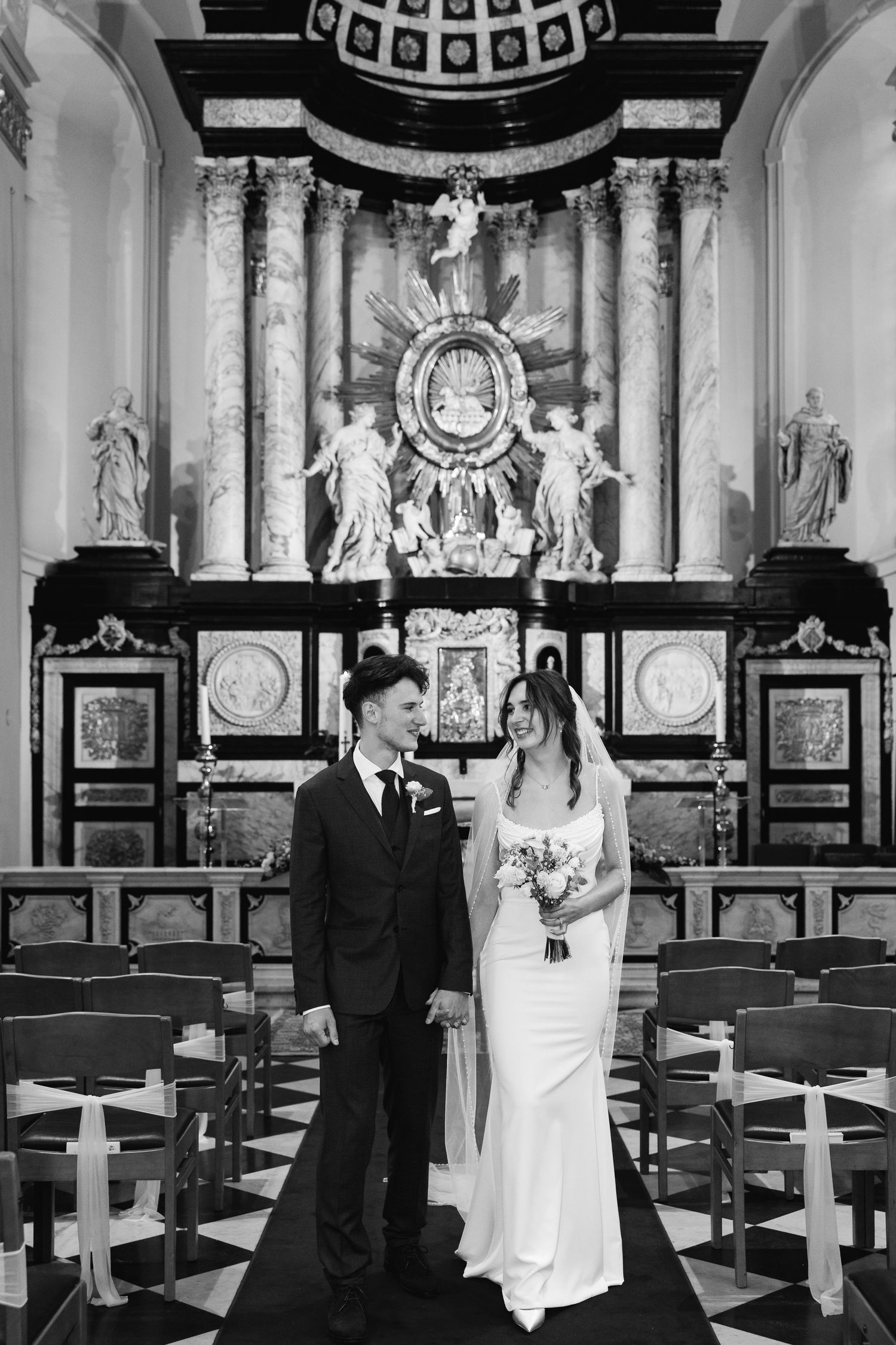 Bride and groom stand together at ornate church altar in black and white wedding portrait.